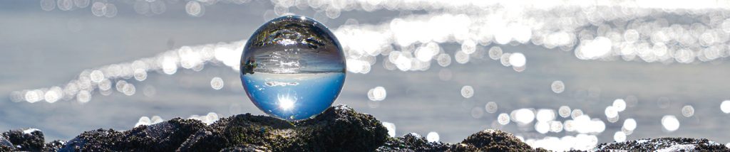 Image of crystal ball creating an upside down image while balanced on rocks along the seashore.